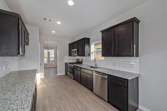 kitchen featuring stainless steel appliances, decorative backsplash, sink, light stone countertops, and light wood-type flooring