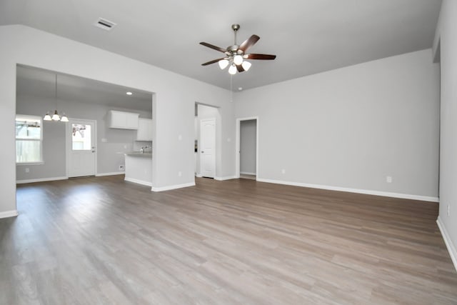 unfurnished living room featuring ceiling fan with notable chandelier, wood-type flooring, and lofted ceiling