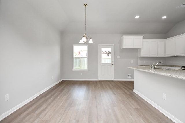 kitchen with white cabinetry, backsplash, light wood-type flooring, light stone countertops, and vaulted ceiling