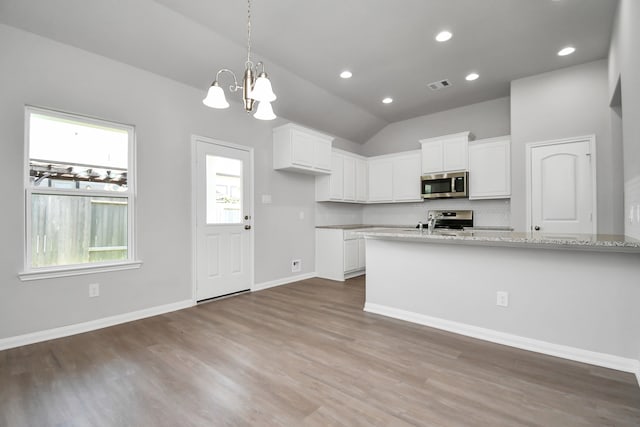 kitchen featuring stainless steel appliances, white cabinetry, light stone counters, and vaulted ceiling