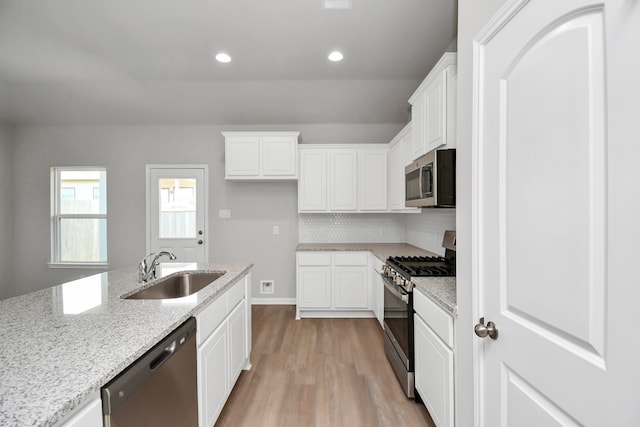 kitchen with stainless steel appliances, light stone counters, sink, white cabinetry, and light hardwood / wood-style flooring