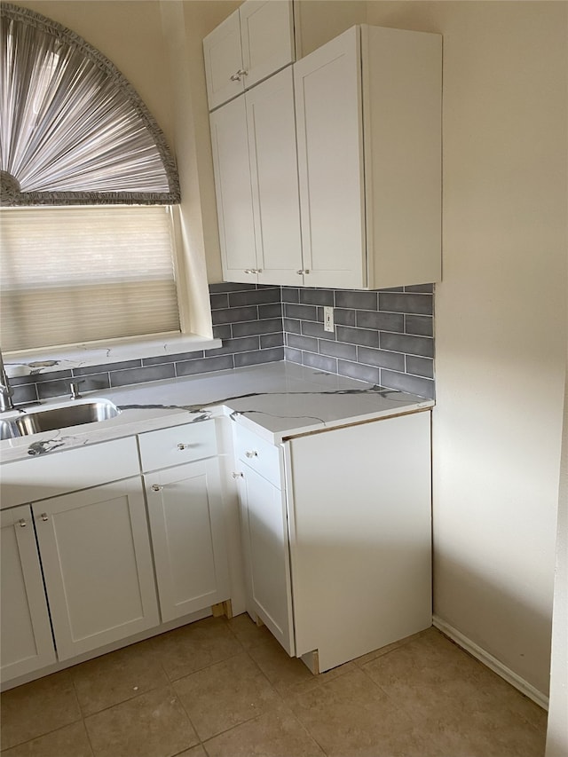 kitchen with backsplash, white cabinetry, light tile patterned floors, and light stone counters