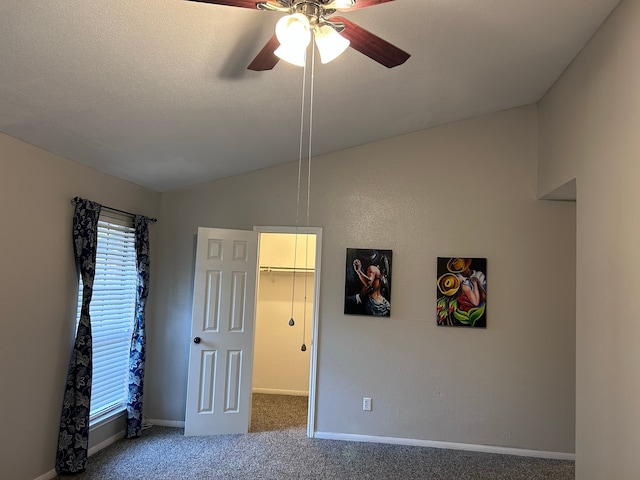 unfurnished bedroom with lofted ceiling, a walk in closet, ceiling fan, carpet floors, and a closet