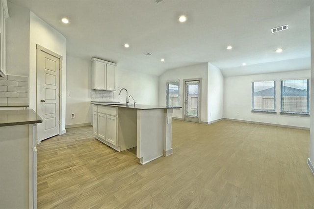 kitchen with backsplash, a kitchen island with sink, sink, light hardwood / wood-style floors, and white cabinetry