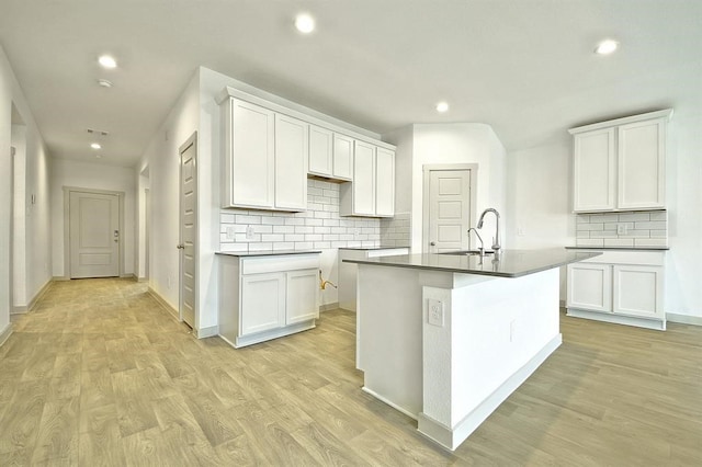 kitchen featuring light wood-type flooring, tasteful backsplash, a kitchen island with sink, sink, and white cabinets