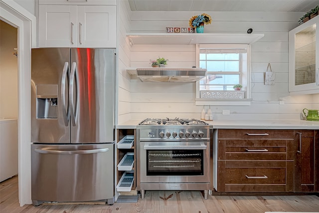 kitchen with stainless steel appliances, white cabinetry, wooden walls, wood ceiling, and light hardwood / wood-style flooring