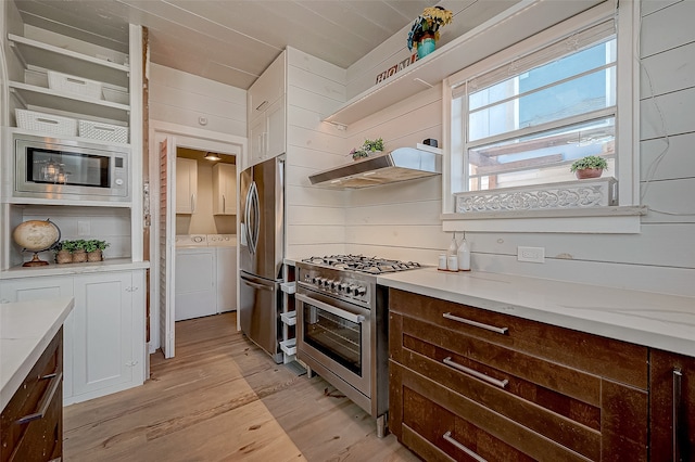 kitchen with stainless steel appliances, light hardwood / wood-style floors, white cabinets, wood walls, and washer and dryer