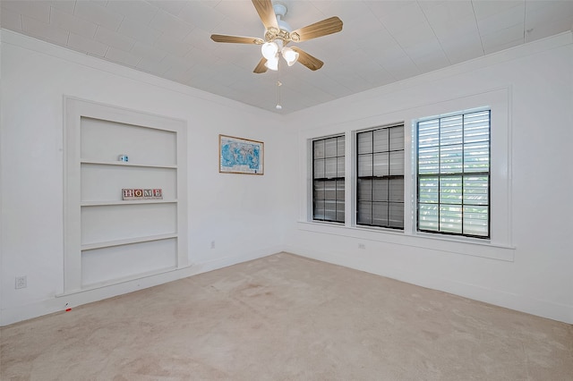 carpeted empty room with ceiling fan, built in features, and crown molding