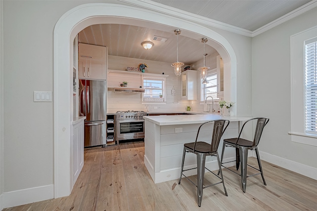 kitchen featuring stainless steel appliances, kitchen peninsula, a breakfast bar area, hanging light fixtures, and white cabinets