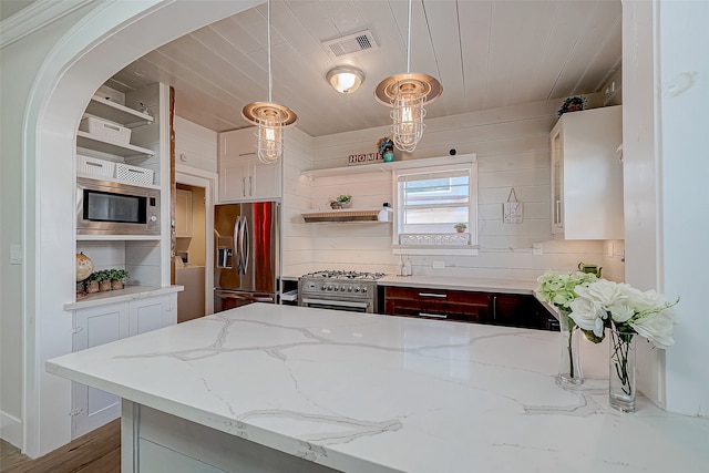 kitchen with light hardwood / wood-style floors, wood walls, light stone countertops, pendant lighting, and appliances with stainless steel finishes