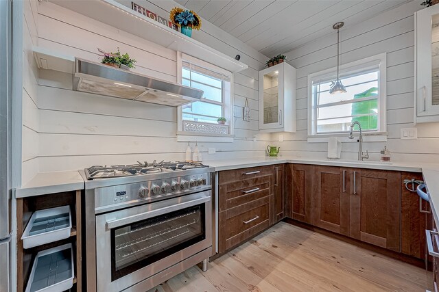 kitchen with wooden walls, range with two ovens, light hardwood / wood-style flooring, and sink