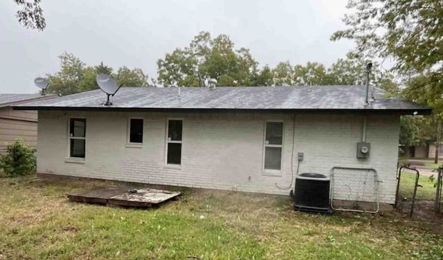 rear view of property with central air condition unit and a lawn