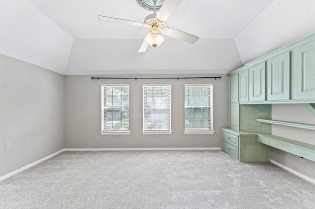 unfurnished office with light colored carpet, built in desk, ceiling fan, and vaulted ceiling