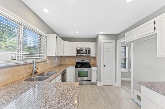 kitchen with stainless steel appliances, light stone counters, white cabinets, sink, and light wood-type flooring