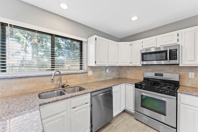 kitchen featuring tasteful backsplash, light stone counters, white cabinetry, appliances with stainless steel finishes, and sink