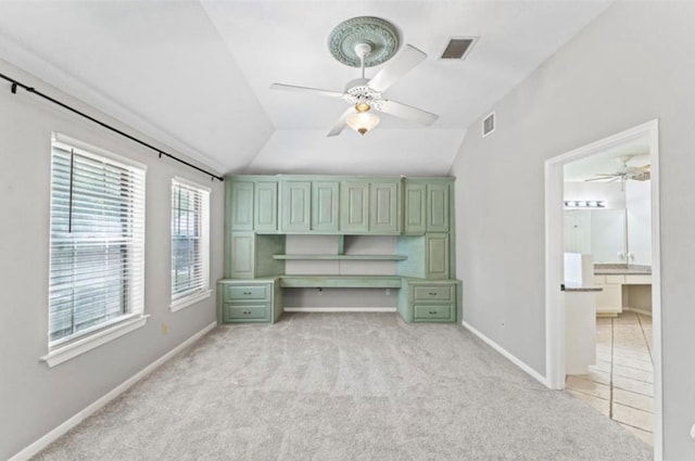 unfurnished bedroom with built in desk, ensuite bath, vaulted ceiling, light colored carpet, and ceiling fan