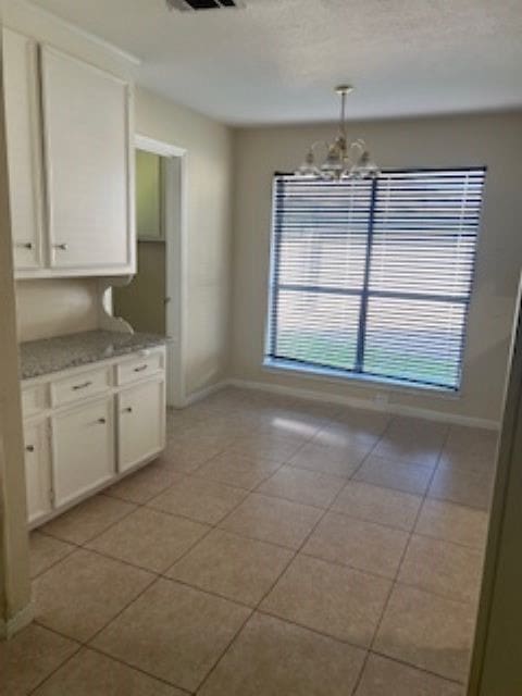 kitchen with an inviting chandelier, light tile patterned floors, light stone countertops, pendant lighting, and white cabinetry