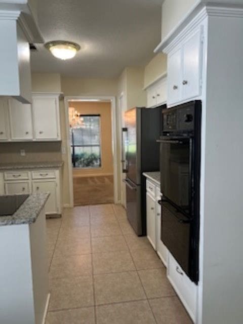 kitchen featuring light tile patterned flooring, stainless steel refrigerator, white cabinetry, and light stone counters