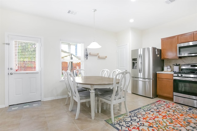 kitchen featuring backsplash, appliances with stainless steel finishes, light tile patterned flooring, and hanging light fixtures