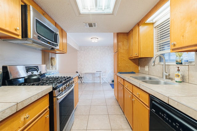 kitchen featuring appliances with stainless steel finishes, sink, light tile patterned floors, and a textured ceiling