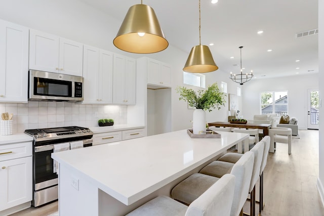 kitchen with light hardwood / wood-style floors, white cabinetry, appliances with stainless steel finishes, hanging light fixtures, and a kitchen island