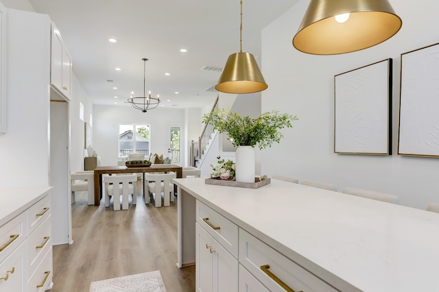 kitchen with white cabinets, light wood-type flooring, pendant lighting, and an inviting chandelier