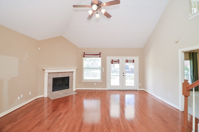 unfurnished living room featuring high vaulted ceiling, french doors, ceiling fan, light wood-type flooring, and a tiled fireplace