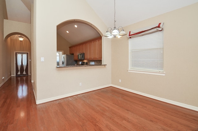 interior space with a notable chandelier, high vaulted ceiling, hardwood / wood-style flooring, appliances with stainless steel finishes, and decorative light fixtures