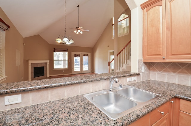 kitchen featuring decorative backsplash, light brown cabinetry, ceiling fan with notable chandelier, sink, and high vaulted ceiling