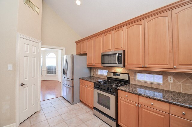 kitchen featuring decorative backsplash, appliances with stainless steel finishes, dark stone counters, light tile patterned floors, and high vaulted ceiling