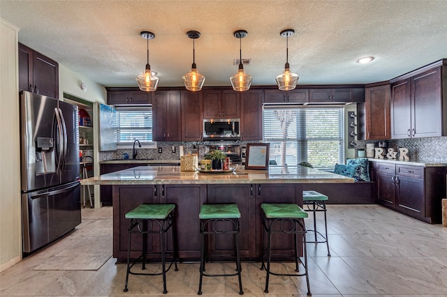 kitchen with stainless steel appliances, a kitchen island, hanging light fixtures, and a healthy amount of sunlight