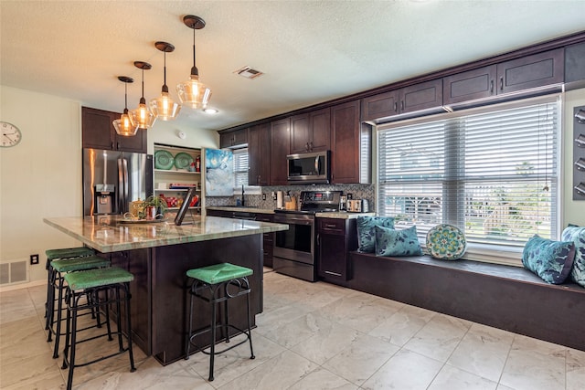 kitchen with light stone countertops, tasteful backsplash, dark brown cabinets, stainless steel appliances, and hanging light fixtures