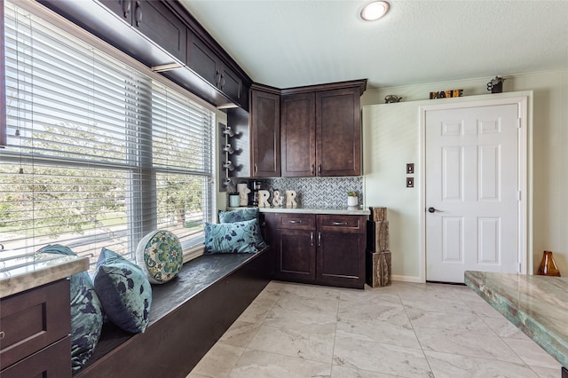 kitchen featuring backsplash, dark brown cabinets, a textured ceiling, and ornamental molding