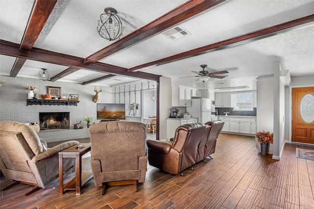 living room with a brick fireplace, dark hardwood / wood-style flooring, a textured ceiling, and beam ceiling