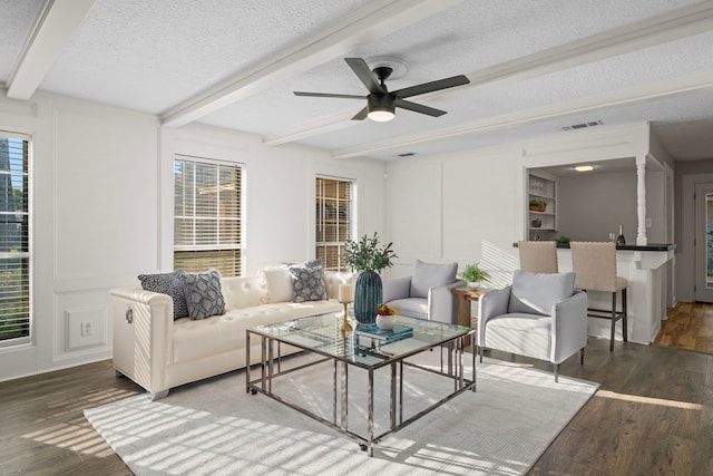 living room featuring ceiling fan, beamed ceiling, dark wood-type flooring, and a textured ceiling