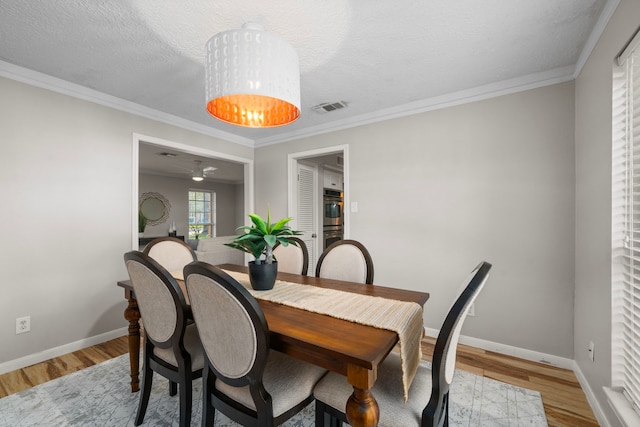 dining space with ornamental molding, a textured ceiling, and light hardwood / wood-style flooring