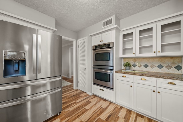 kitchen featuring decorative backsplash, appliances with stainless steel finishes, light hardwood / wood-style flooring, dark stone countertops, and white cabinetry