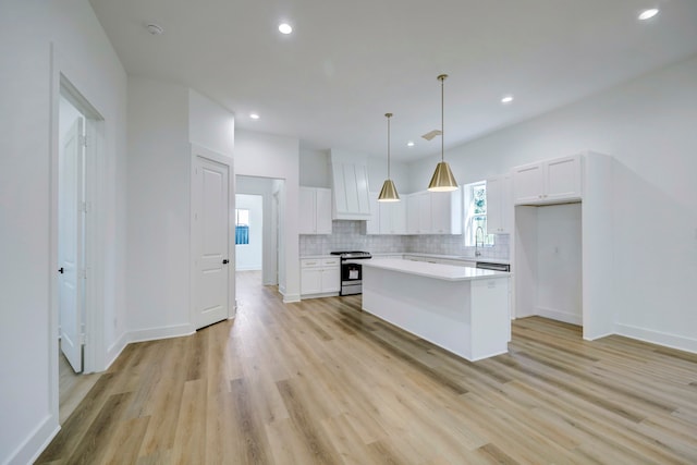 kitchen with a kitchen island, pendant lighting, white cabinets, gas range, and light hardwood / wood-style flooring