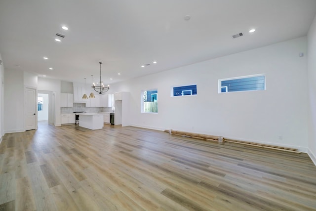 unfurnished living room with an inviting chandelier and light hardwood / wood-style flooring