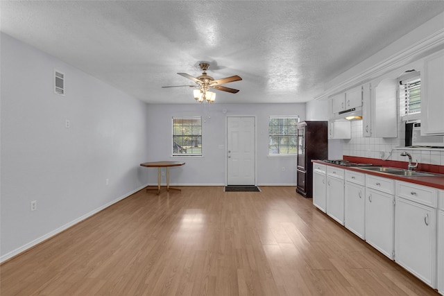 kitchen featuring black refrigerator, light hardwood / wood-style flooring, ceiling fan, white cabinetry, and decorative backsplash