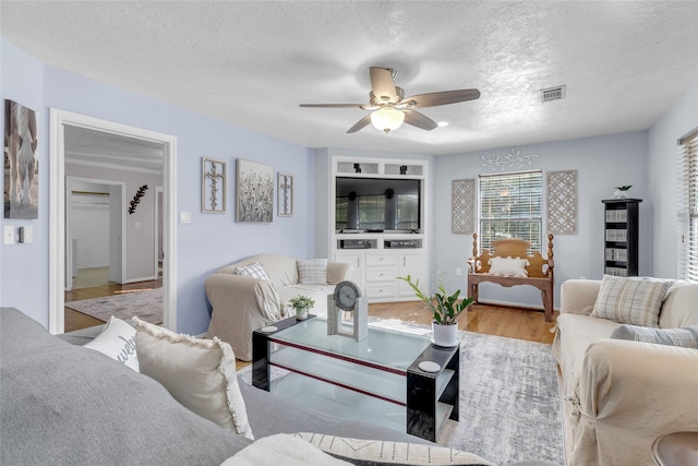 living room with built in shelves, a textured ceiling, light hardwood / wood-style flooring, and ceiling fan