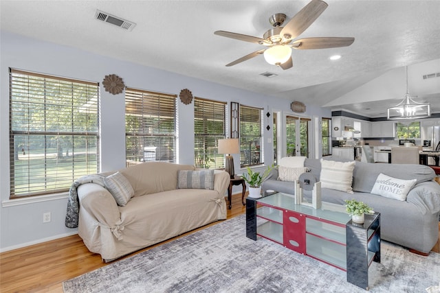 living room featuring ceiling fan with notable chandelier, a textured ceiling, lofted ceiling, and light wood-type flooring