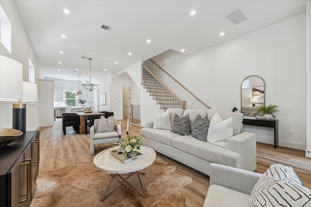 living room with a towering ceiling, a chandelier, and light hardwood / wood-style flooring