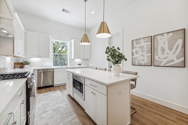 kitchen featuring a kitchen island, appliances with stainless steel finishes, hanging light fixtures, hardwood / wood-style flooring, and white cabinets