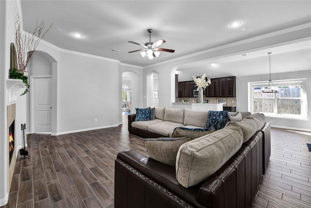 living room featuring ornamental molding, dark wood-type flooring, and ceiling fan with notable chandelier