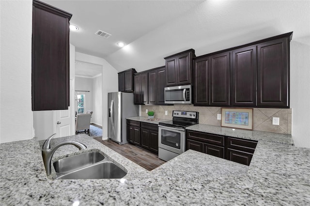 kitchen featuring lofted ceiling, sink, wood-type flooring, appliances with stainless steel finishes, and backsplash