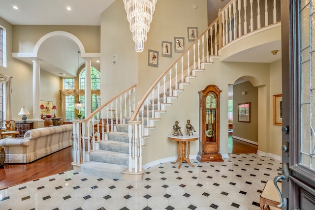 foyer featuring hardwood / wood-style floors, a towering ceiling, a chandelier, and ornate columns