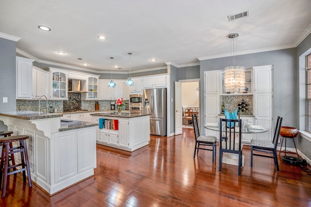 kitchen with stainless steel appliances, a center island, white cabinets, wall chimney range hood, and pendant lighting