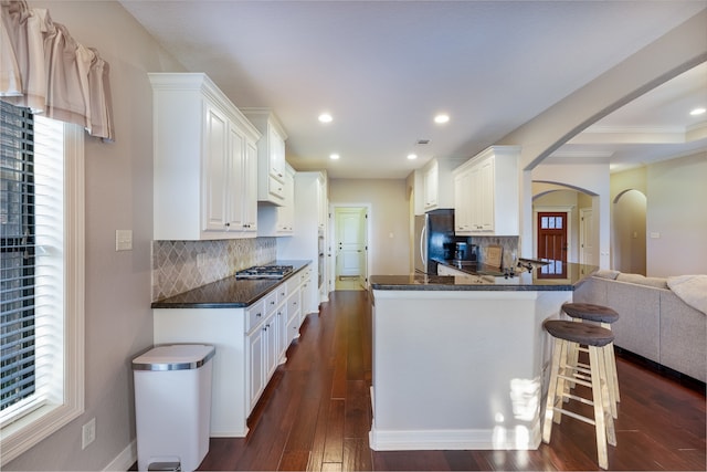 kitchen with stainless steel appliances, white cabinetry, kitchen peninsula, backsplash, and dark wood-type flooring