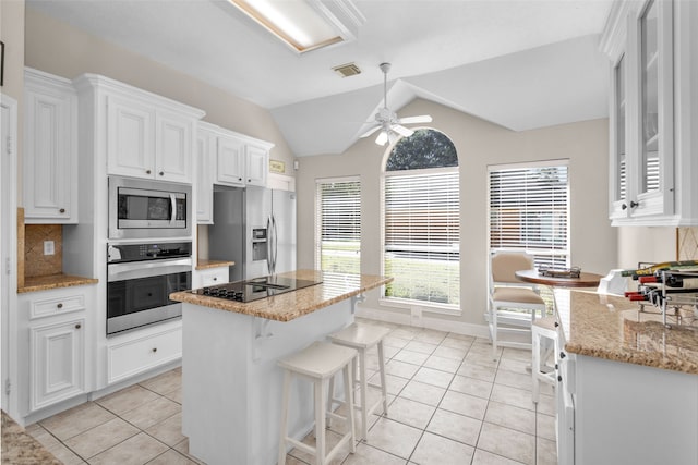 kitchen with vaulted ceiling, ceiling fan, appliances with stainless steel finishes, light tile patterned flooring, and white cabinetry